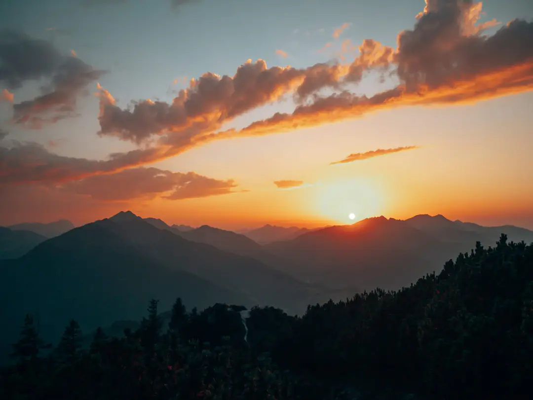 The sun setting behind layered alpine ridges and dark spruce forest in the Bavarian Alps