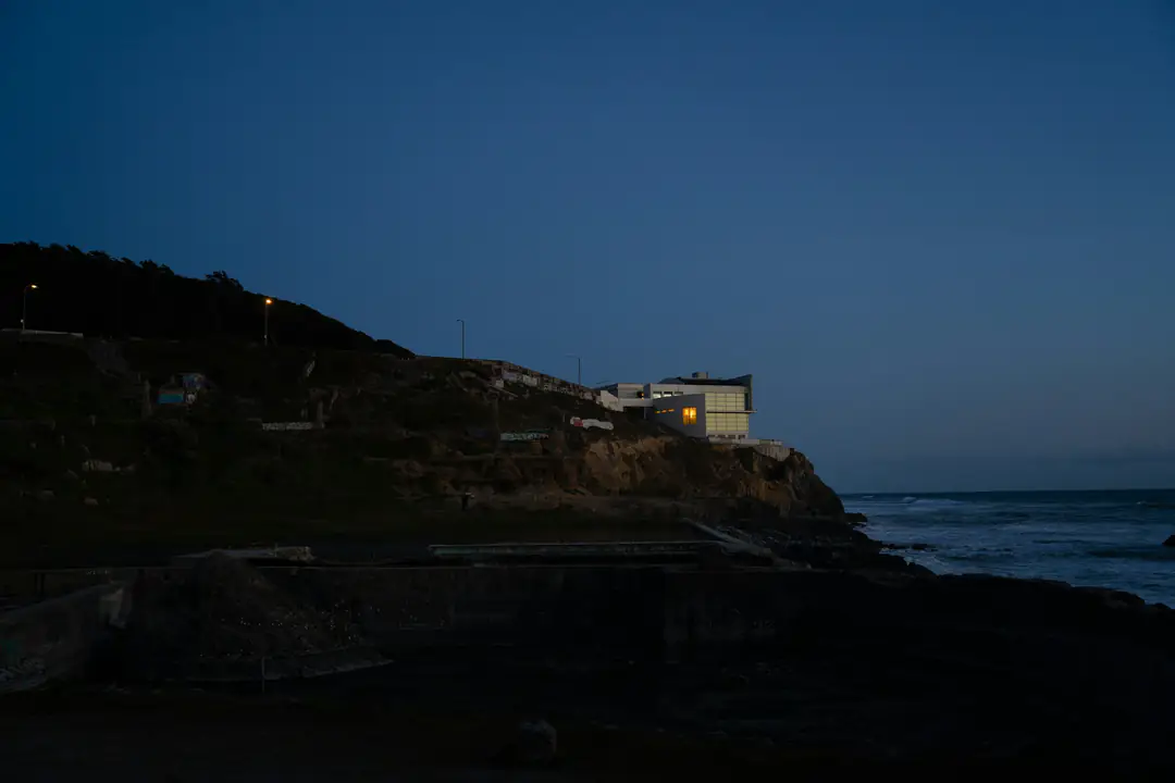 A house on a dark sea cliff, its windows lit at blue hour