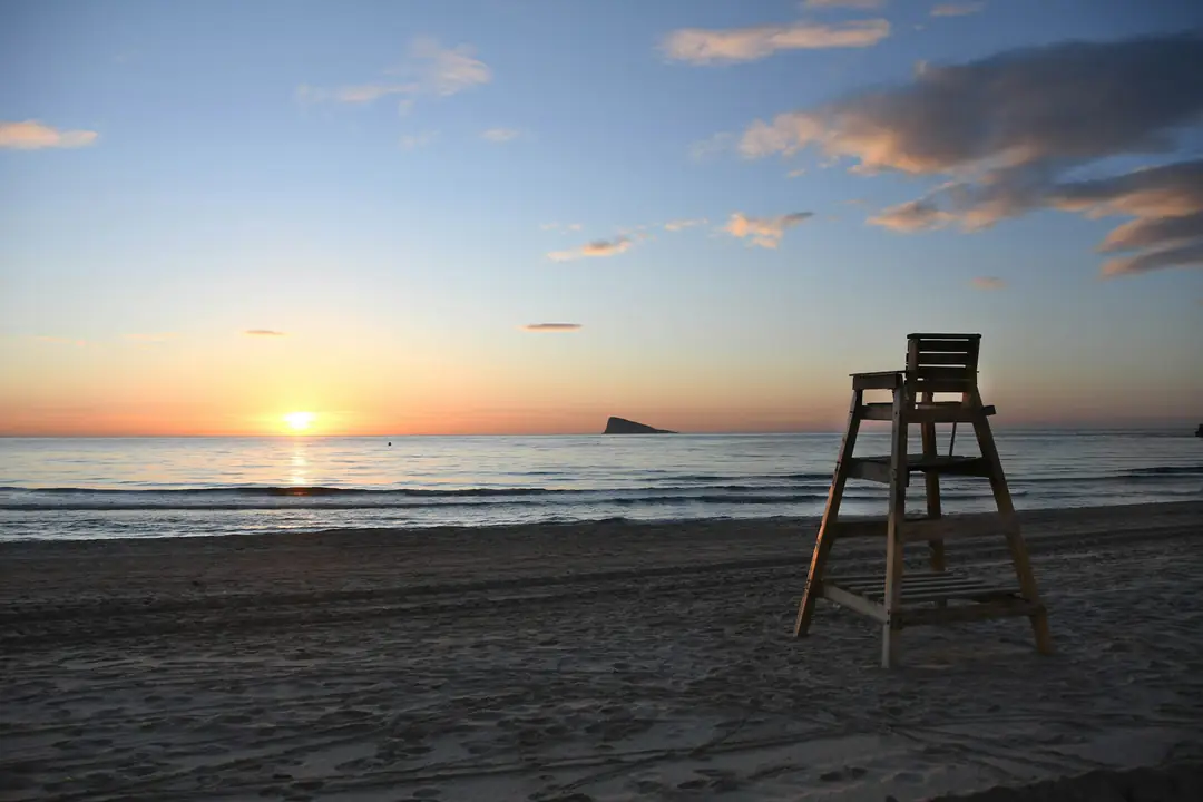 An empty lifeguard chair on a quiet beach in Benidorm as the sun meets the sea