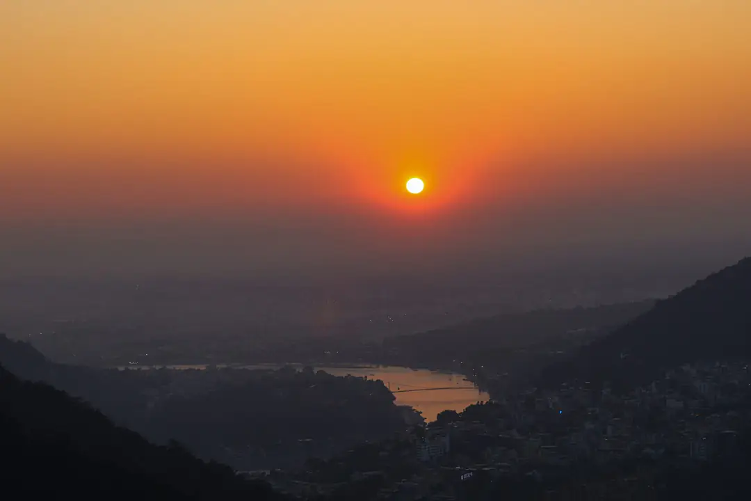 The sun setting through haze over the forested hills and river valley at Rishikesh