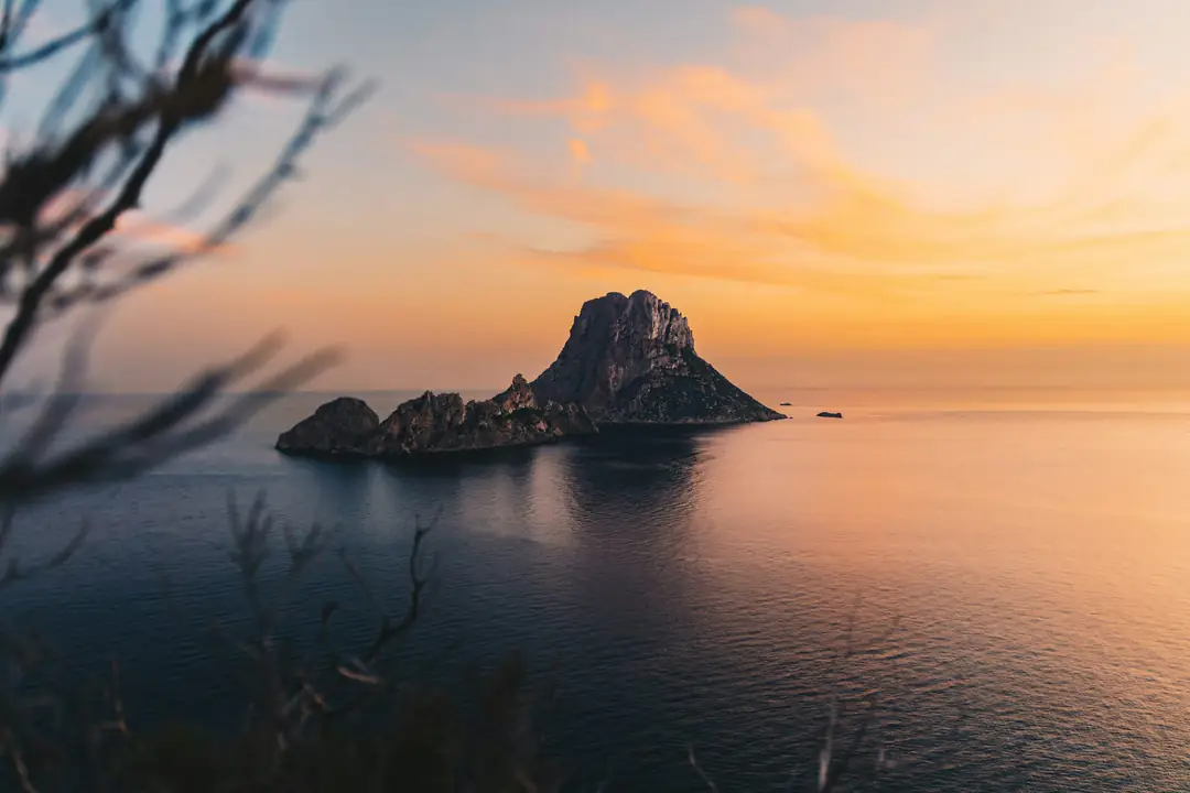 The rock island of Es Vedrà in a calm sea at sunset off the coast of Ibiza