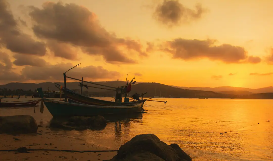 A wooden fishing boat moored in shallow water under a golden Koh Samui sunset