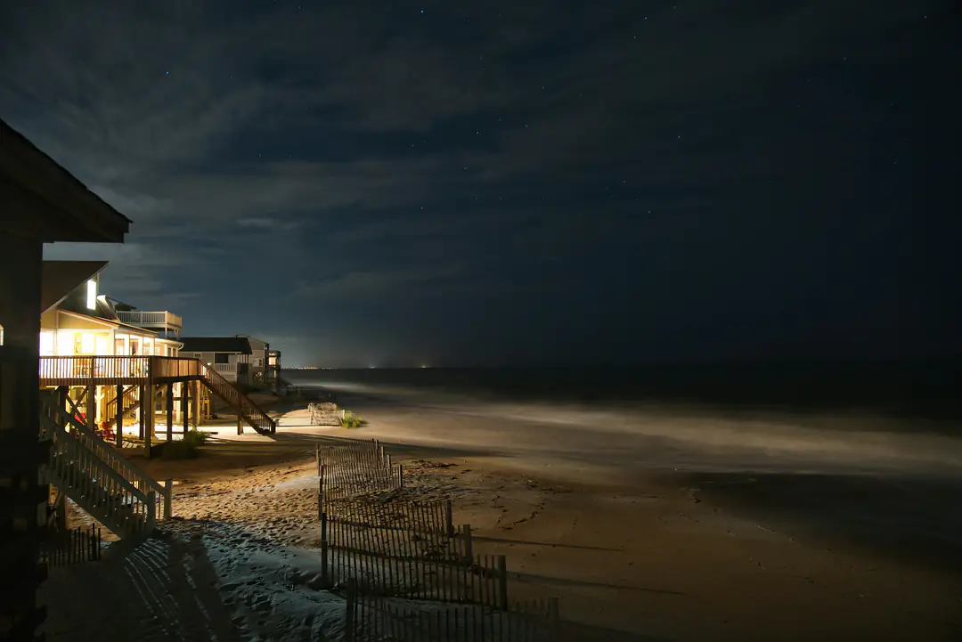 Beach houses with lit windows above the sand at night