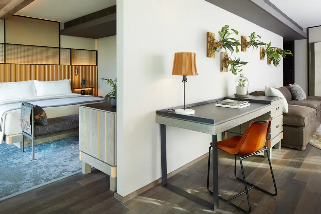 Suite with a bed behind a partition, a desk and leather chair, and staghorn ferns mounted on the wall