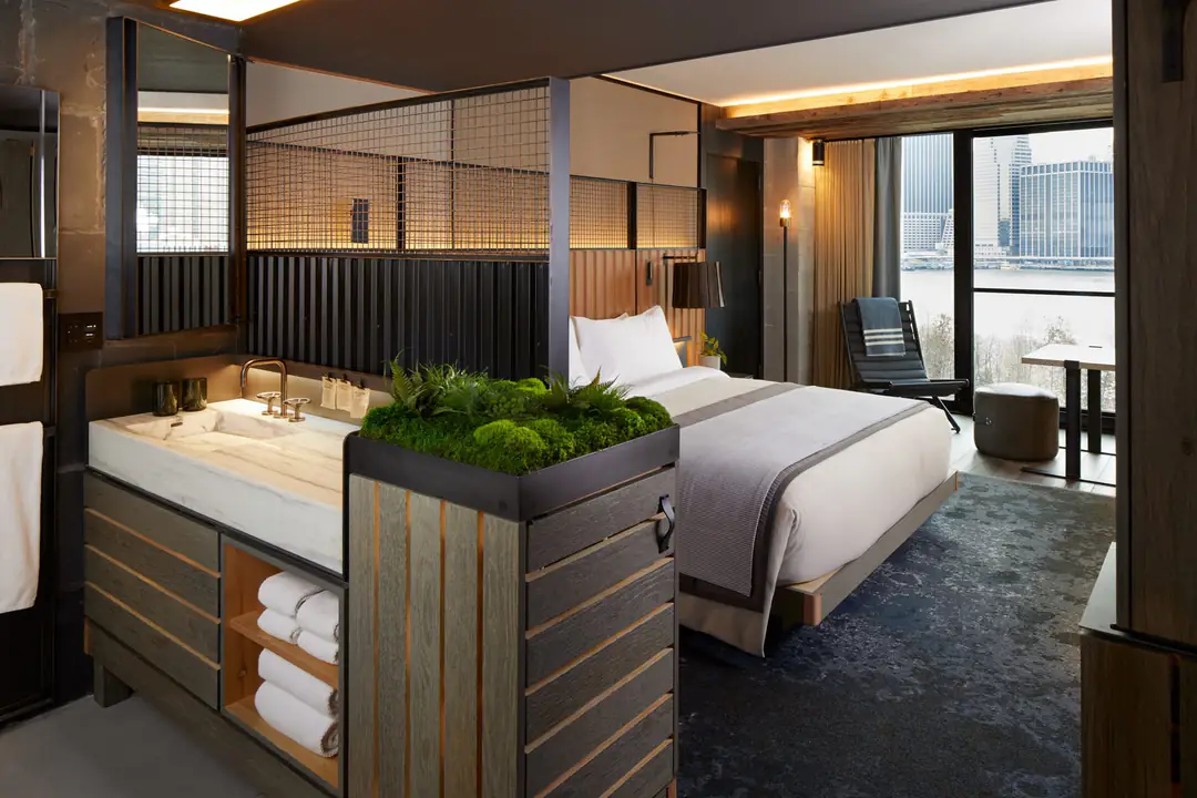 Guest room with a marble sink, a moss planter, a bed and a window onto the East River and Lower Manhattan