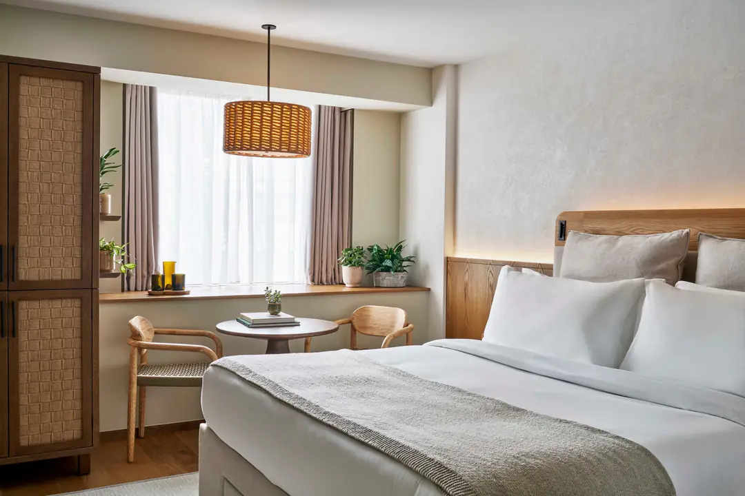 Courtyard King room with oak headboard, woven wardrobe, a round table by the window and potted plants on the sill