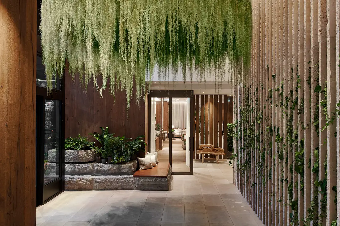 Lobby entrance with hanging moss overhead, rough stone planters, a leather bench and a slatted stone wall with ivy