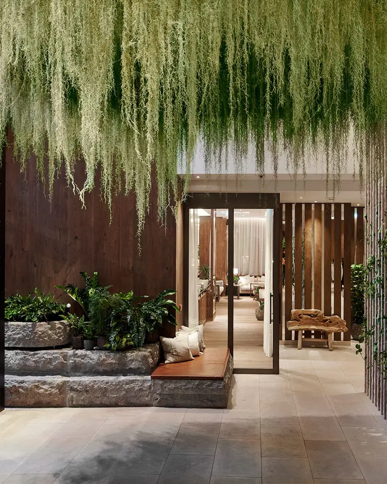Lobby entrance with hanging moss overhead, rough stone planters, a leather bench and a slatted stone wall with ivy