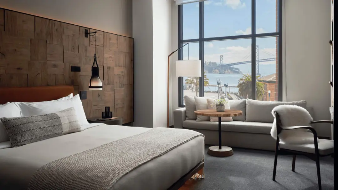 King room with a wood-block headboard wall, sofa and tall window looking over the Embarcadero to the Bay