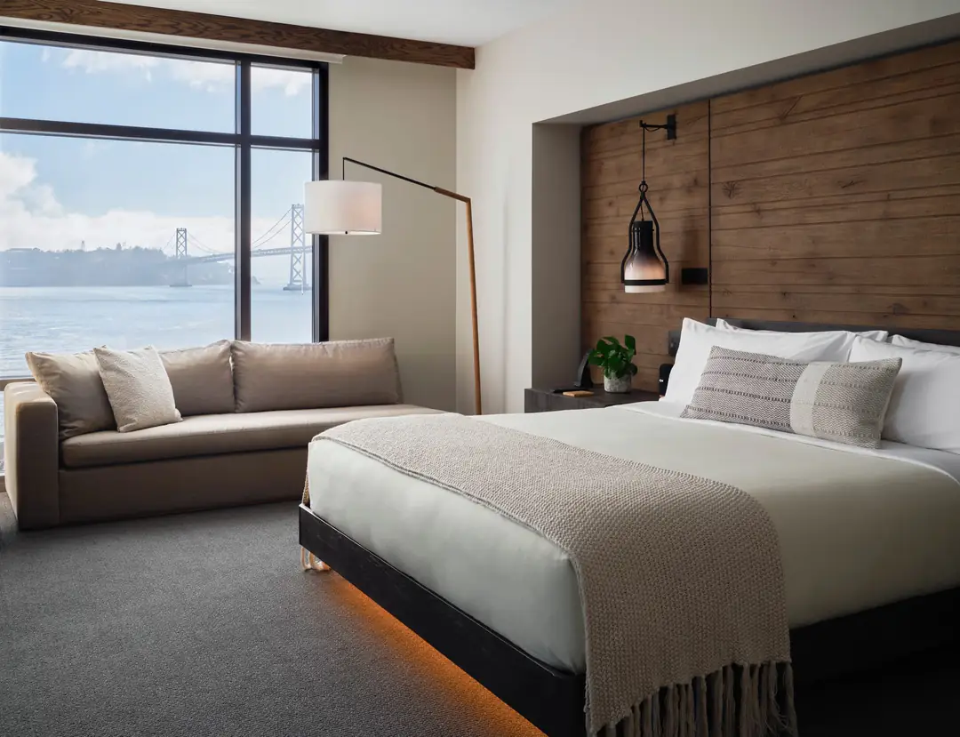 Suite bedroom with a reclaimed-wood headboard wall, a sofa and a large window onto the Bay Bridge