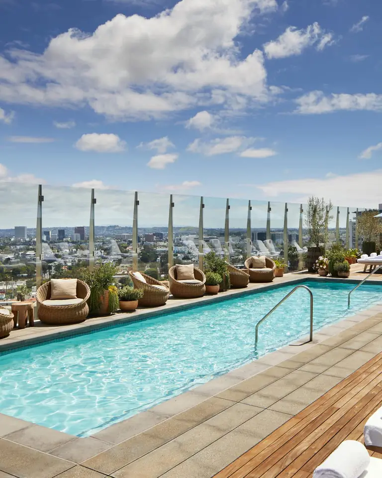 Rooftop pool with white loungers, wicker chairs and a glass rail over the West Hollywood skyline