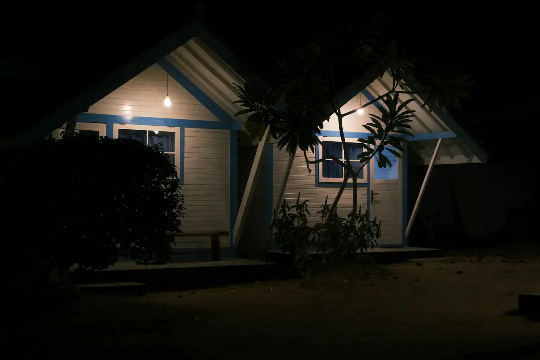 Two small cottages with lit porches among trees at night