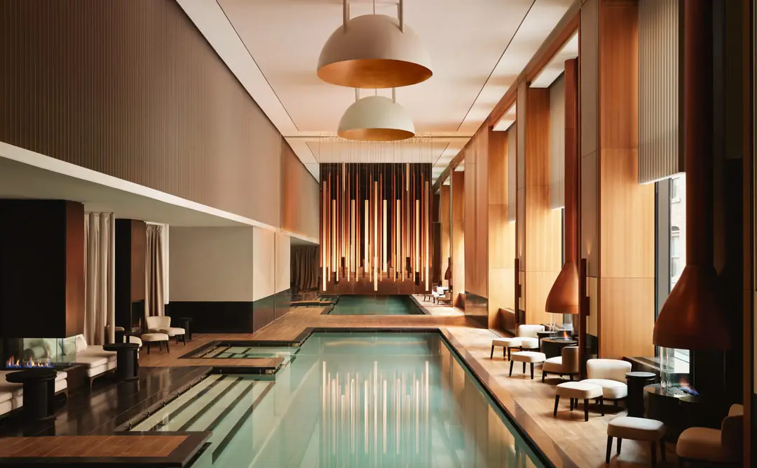 Long indoor spa pool lined with daybeds, hanging copper fireplaces and a curtain of vertical lights at the far end