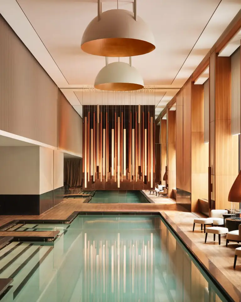 Long indoor spa pool lined with daybeds, hanging copper fireplaces and a curtain of vertical lights at the far end