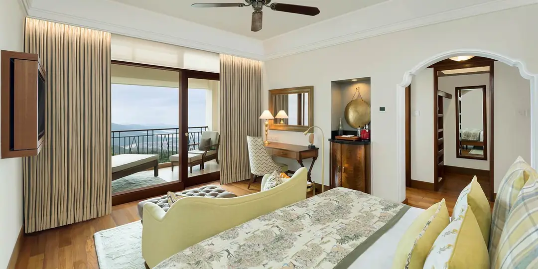 Deluxe room with a bed, a green sofa and wood floors, open to a balcony over the valley
