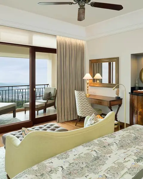 Deluxe room with a bed, a green sofa and wood floors, open to a balcony over the valley