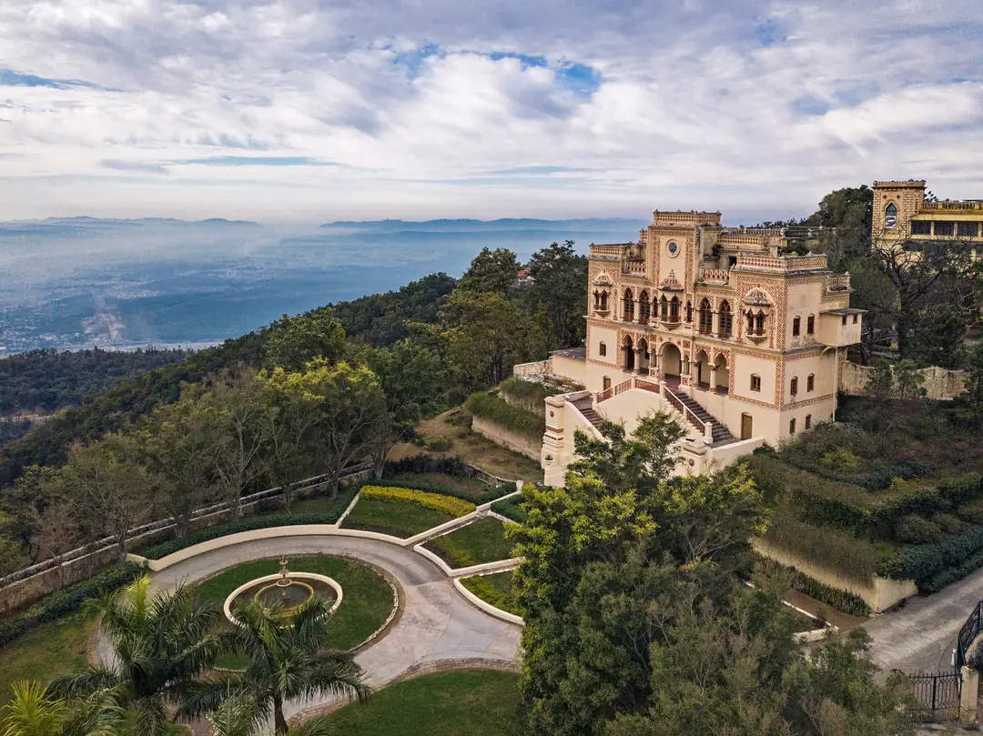 Aerial view of the cream and terracotta Viceregal Palace on a wooded ridge above a hazy valley