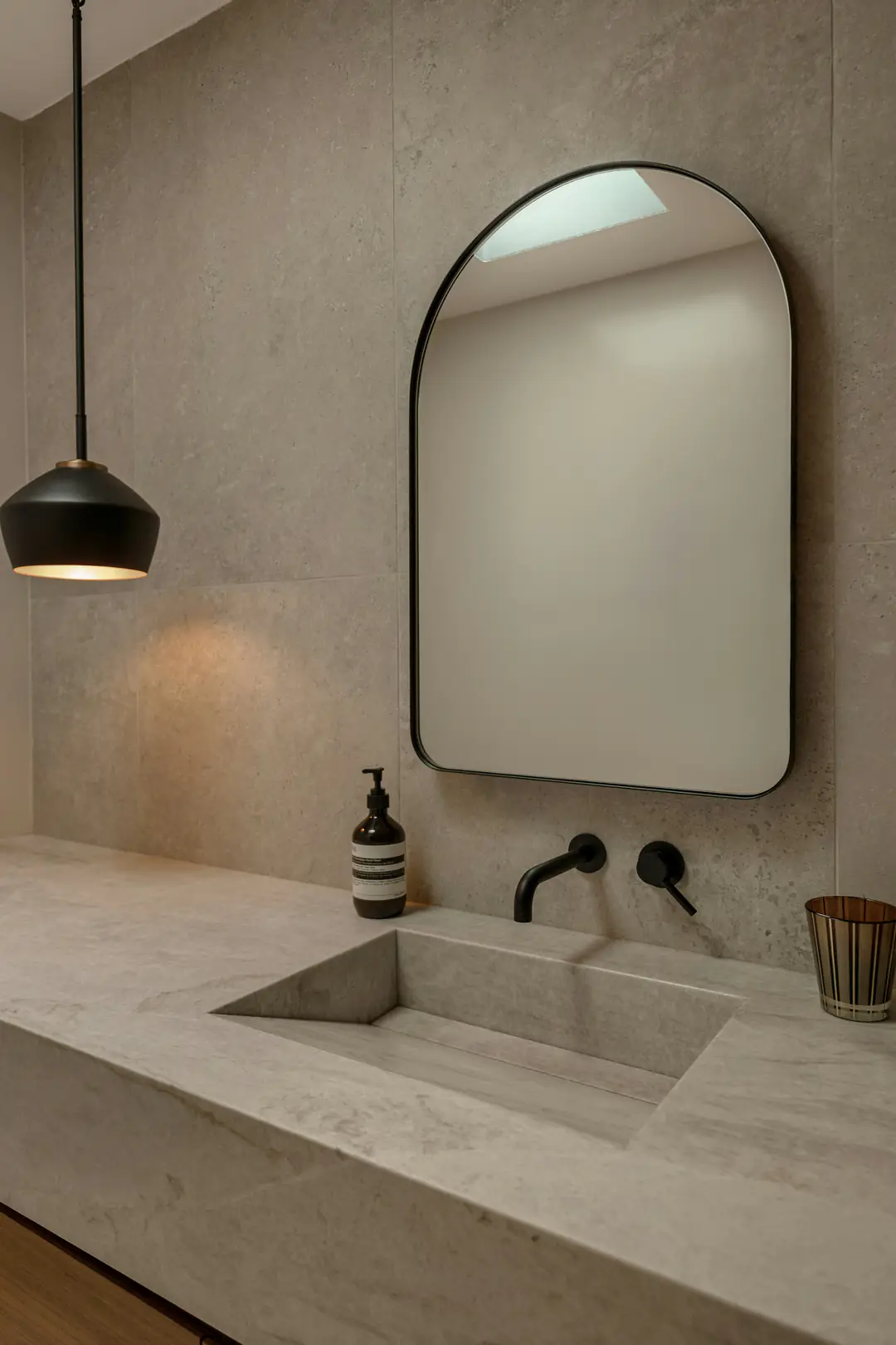 A calm limestone bathroom with an integrated basin and an arched mirror