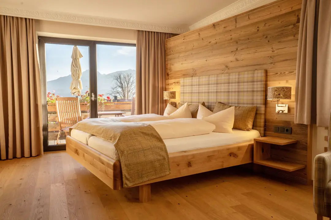 A guest room with an oak bed, plank-wood wall, wood floor and a balcony door facing the mountains