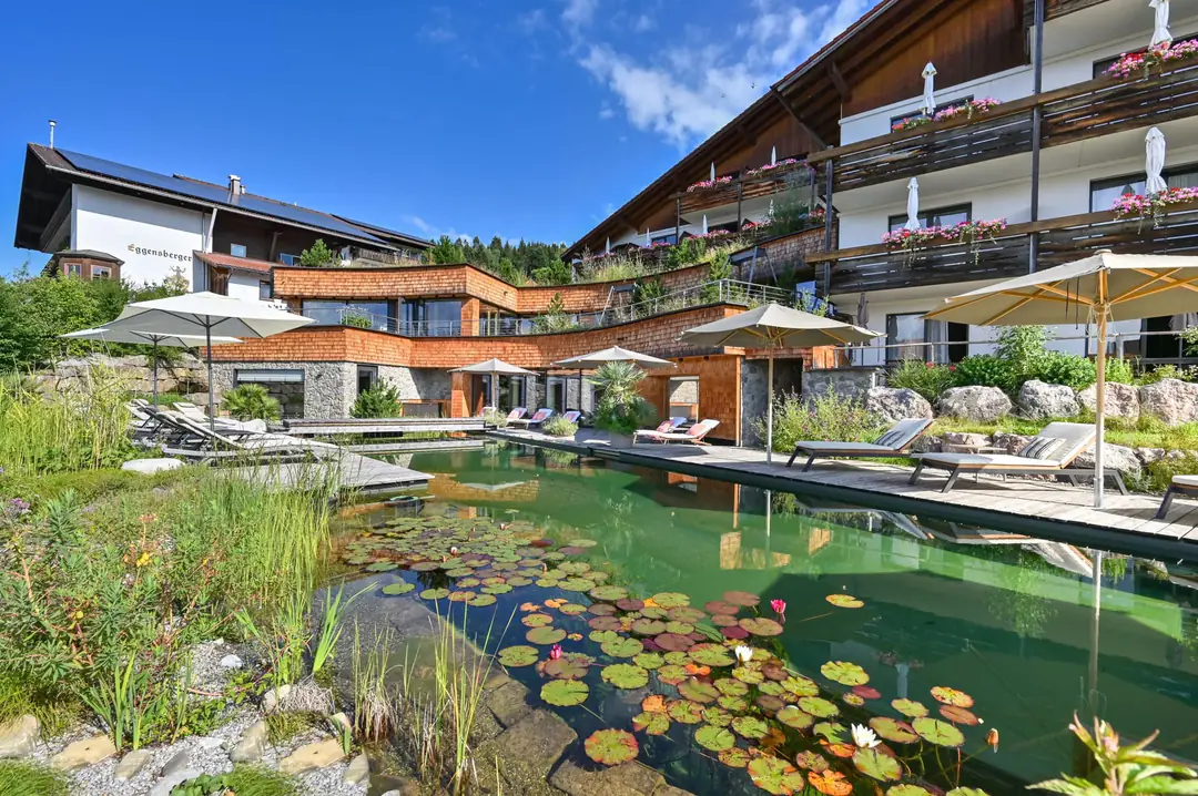 A natural swimming pond with water lilies and sun loungers below the hotel's wood-shingled spa wing and balconies