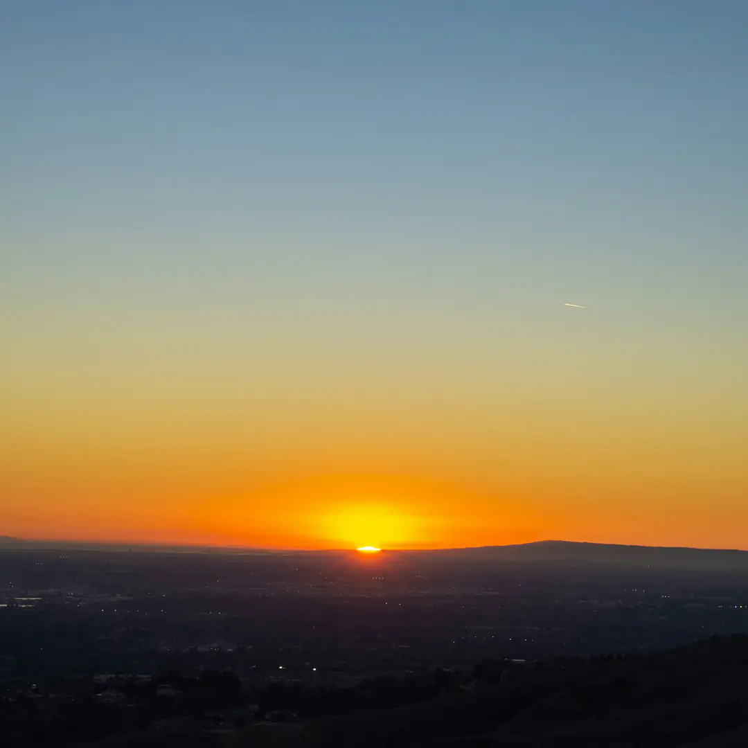 The sun setting orange over a dark valley and far hills