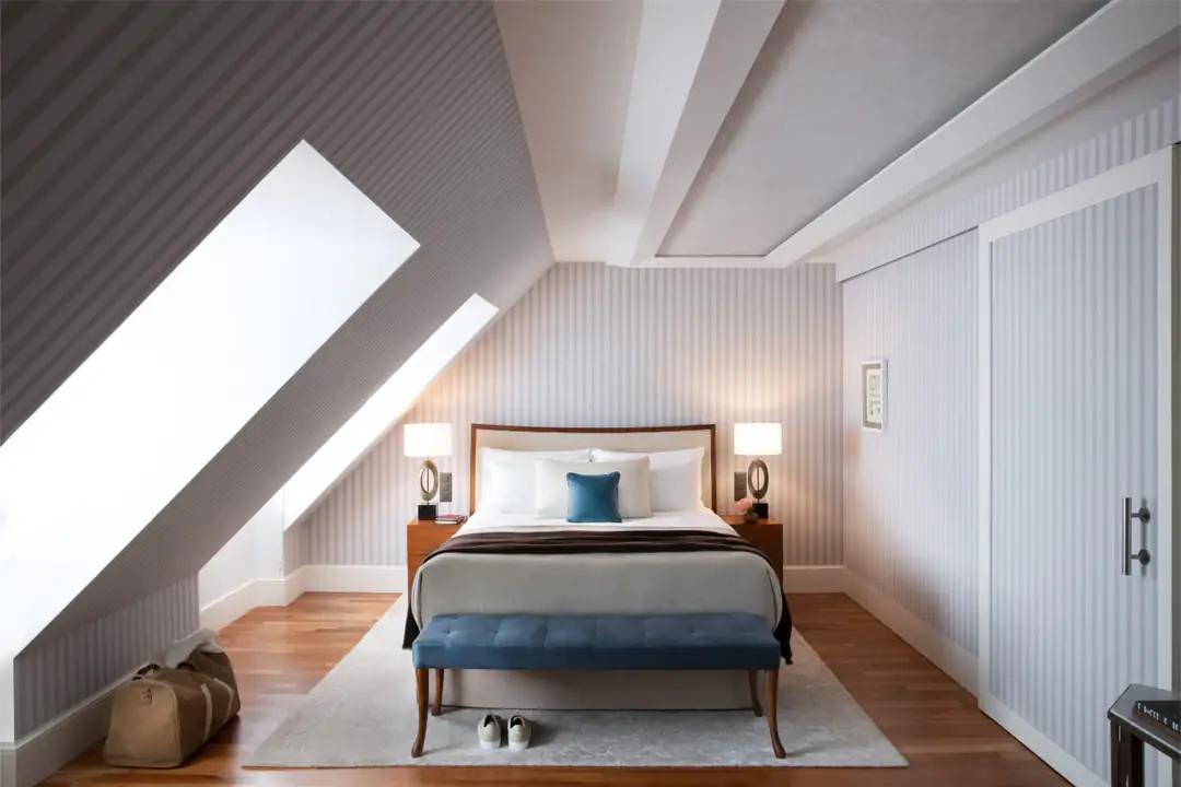 Superior Room under sloping eaves: double bed, striped walls, wooden floor and a blue bench at the foot