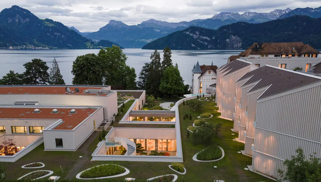 Pale timber-clad new wing and green roof garden of Chenot Palace at dusk, Lake Lucerne and mountains behind