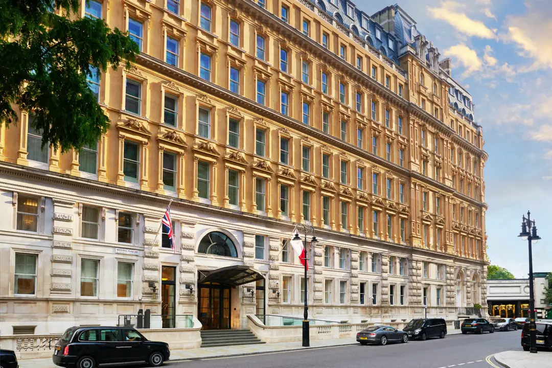 The hotel's cream Victorian stone facade on Whitehall Place, with a glass entrance canopy and a black cab outside