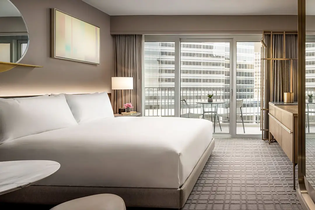 Guest room with a king bed, abstract art above it and glass doors to a balcony with a table