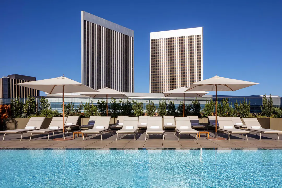 Rooftop pool with white loungers and umbrellas, the twin Century City towers behind