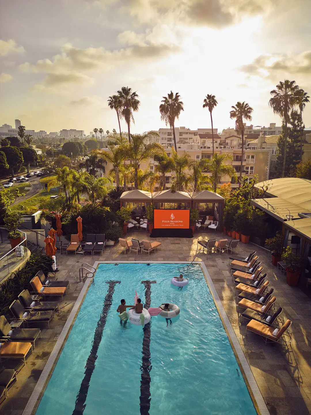 Fourth-floor pool from above at sunset, lined with loungers, cabanas and tall palms