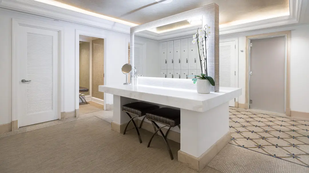 Spa changing area with a lit marble vanity, two stools, an orchid and white lockers