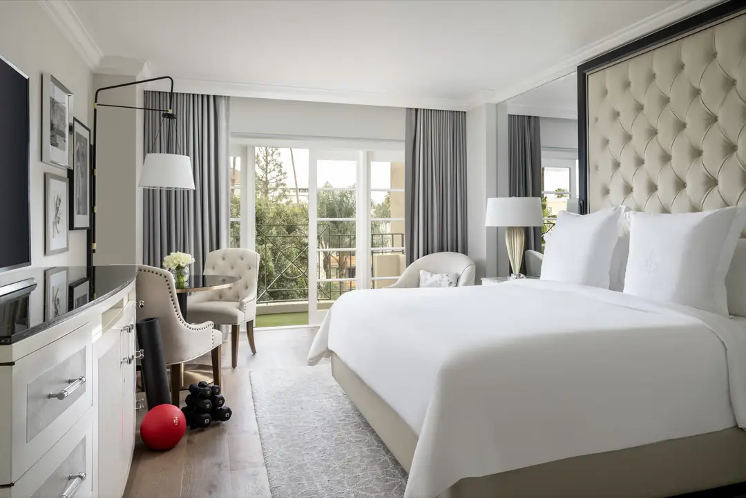 Wellness room with a tufted headboard, white bed, dumbbells and medicine ball, French doors open to a balcony