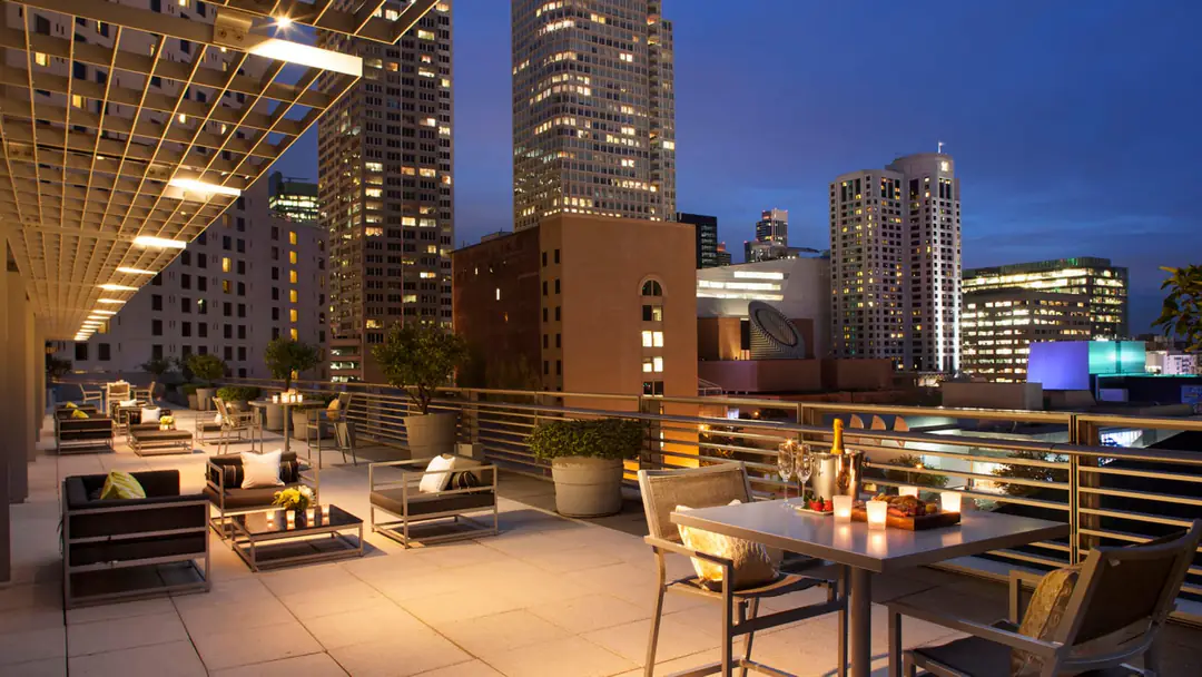 Candlelit rooftop terrace with lounge seating and a table for two, city towers lit up at dusk