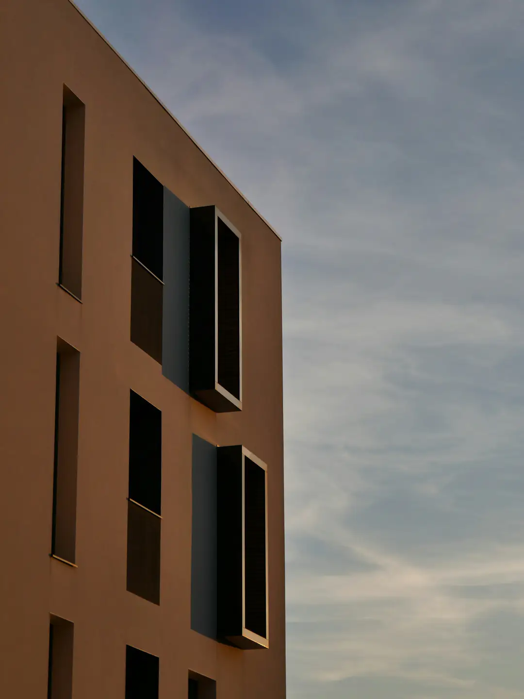 A warm ochre building with deep-set windows against a pale sky