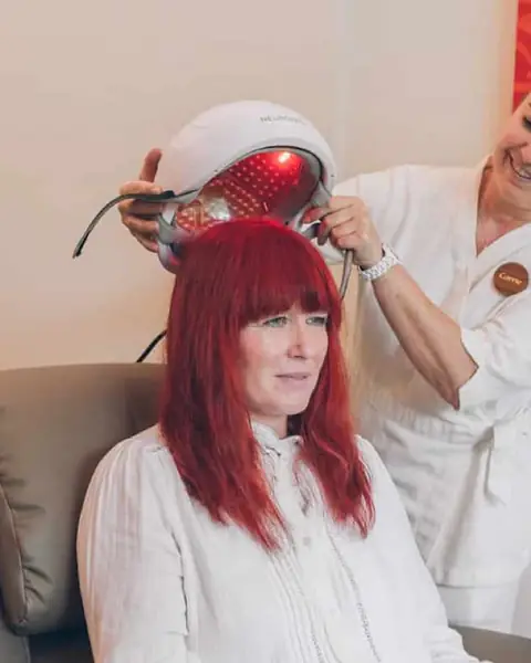 A therapist fits a red-light photobiomodulation helmet on a seated guest in the Cognitive House