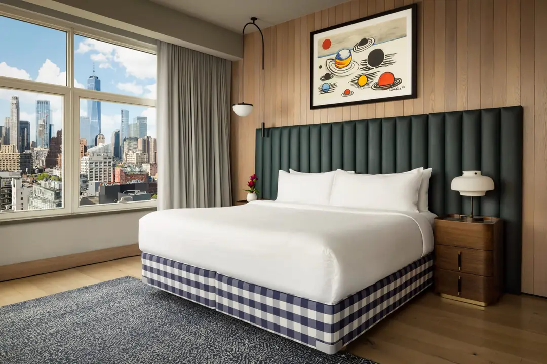 Penthouse bedroom with a blue-and-white check Hästens bed, green padded headboard, wood-panelled wall and oak floor