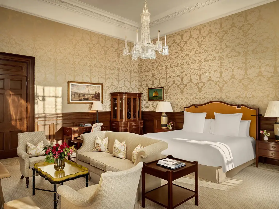Guest room with gold damask walls, oak panelling, a crystal chandelier and a king bed