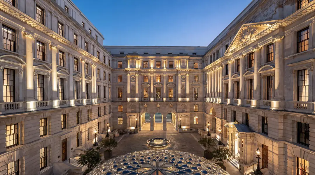 The floodlit stone courtyard of the Old War Office at dusk, with a fountain and glass dome below