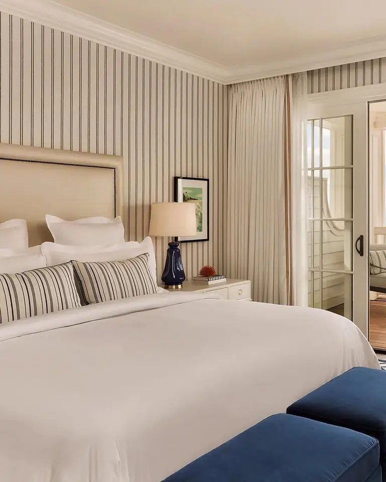 Guestroom with a white king bed, striped walls and open French doors to a terrace above the ocean