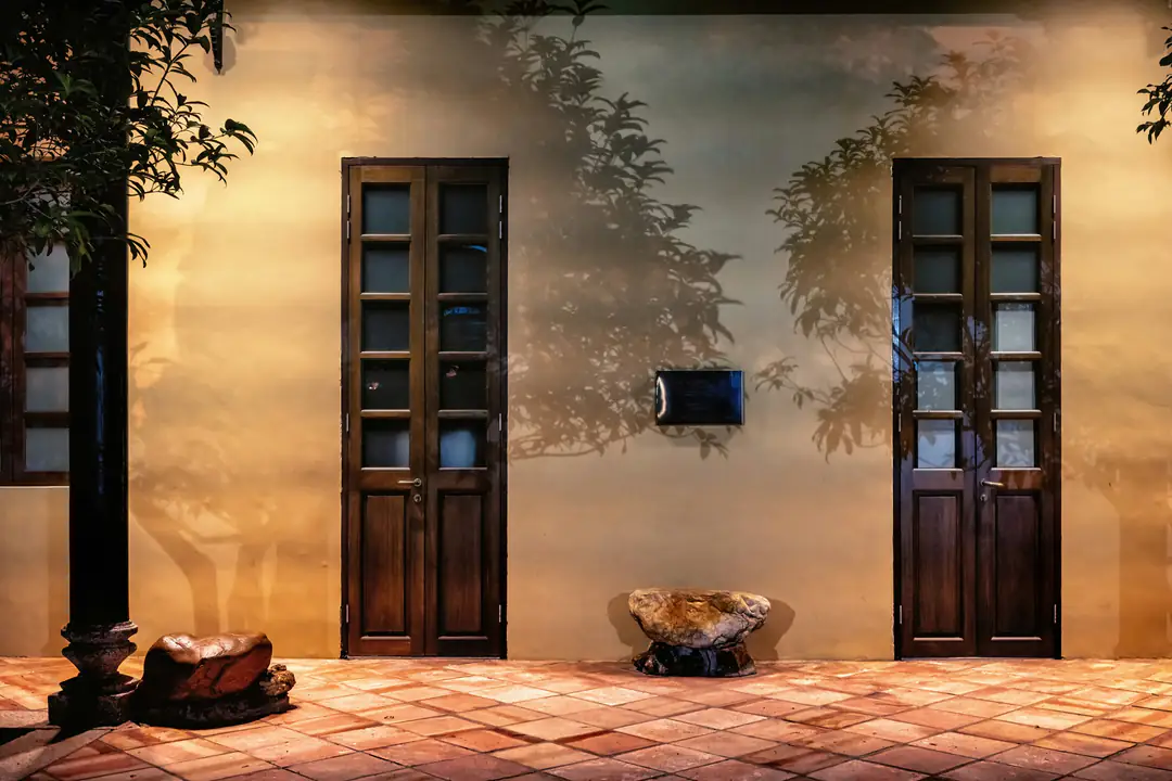 A warm plaster wall lit at night between two tall wooden doors
