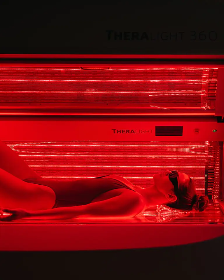 Person lying in a lit TheraLight 360 red-light bed in a dark room, glowing red