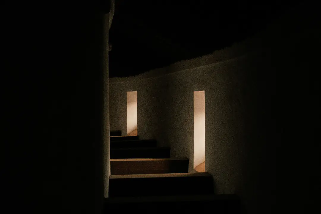 A curved plaster stair in the dark, lit from narrow openings in the wall