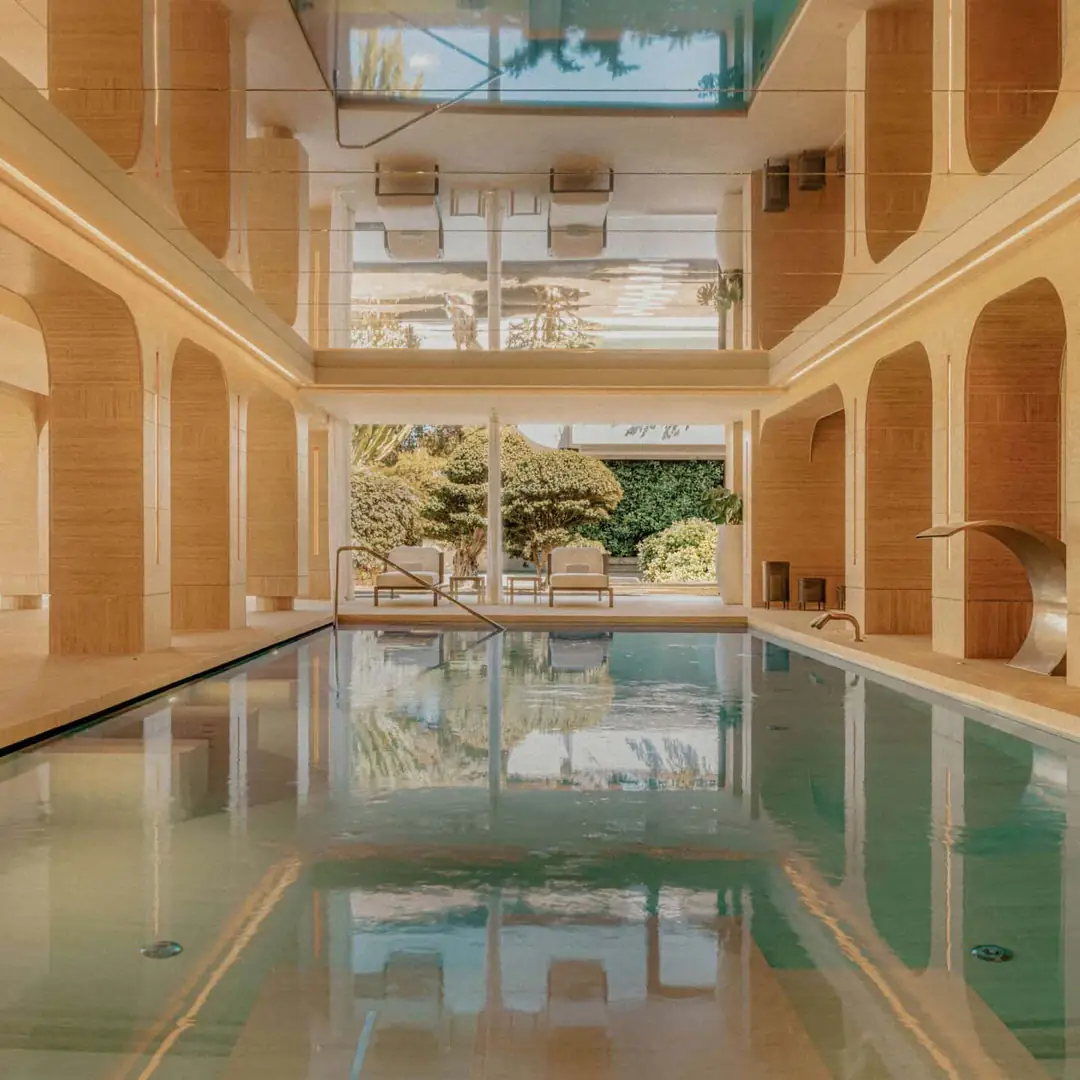 Indoor hydrotherapy pool lined with arched stone niches and a water jet, opening onto a garden