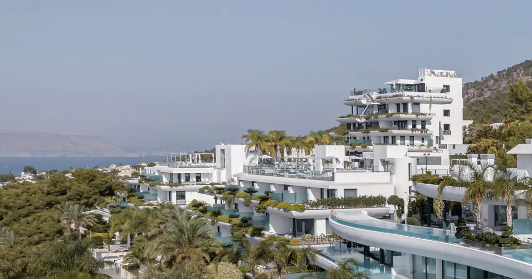 White terraced buildings of SHA among palms and pines on a hillside above Altea Bay