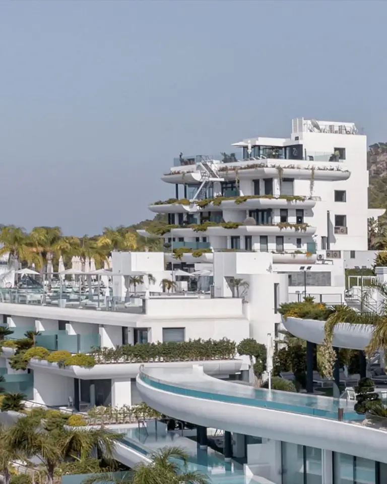 White terraced buildings of SHA among palms and pines on a hillside above Altea Bay