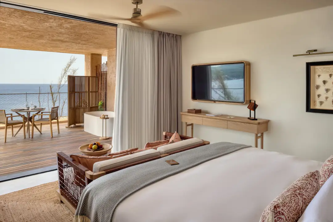 Sea-view room with a made bed in daylight, sheer curtains and a terrace open to the sea