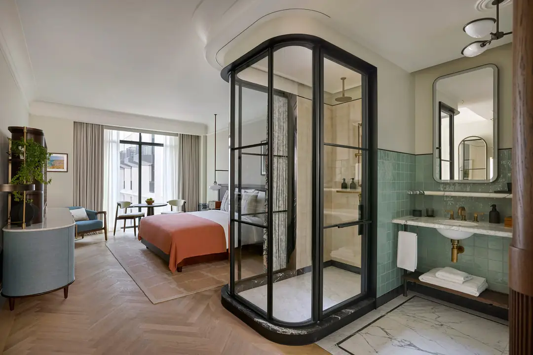 Room with a black-framed glass shower beside the bed, green tiled basin and tall windows