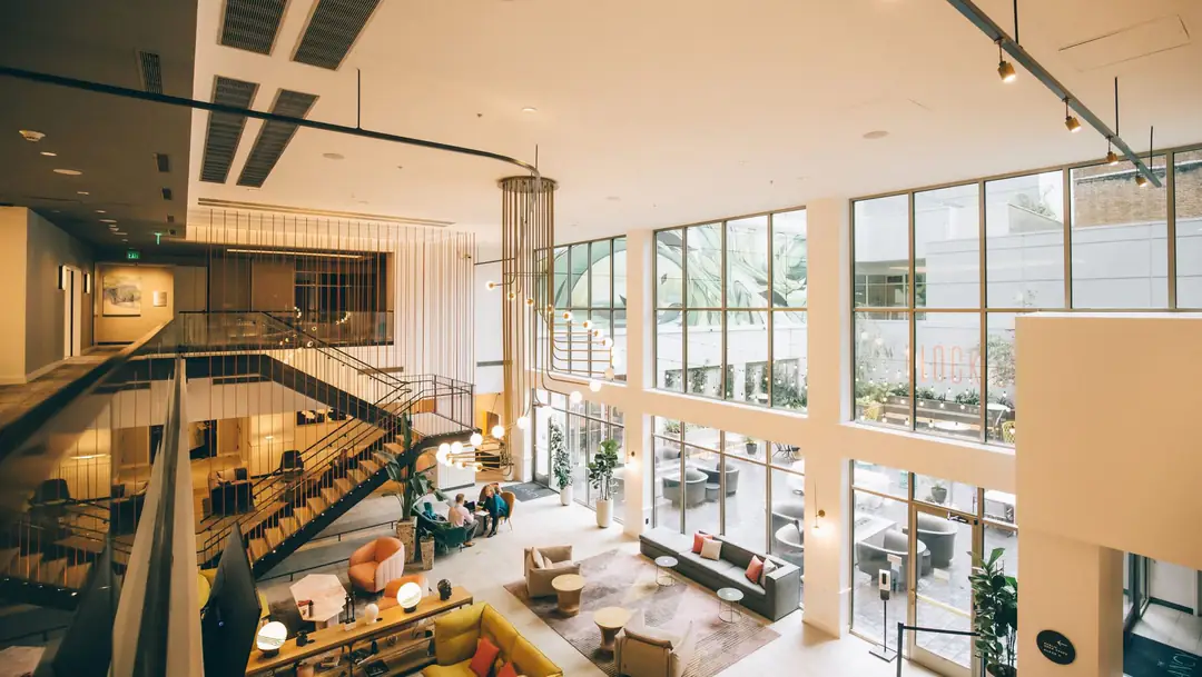 Double-height lobby with a black steel stair, floor-to-ceiling windows and low lounge seating