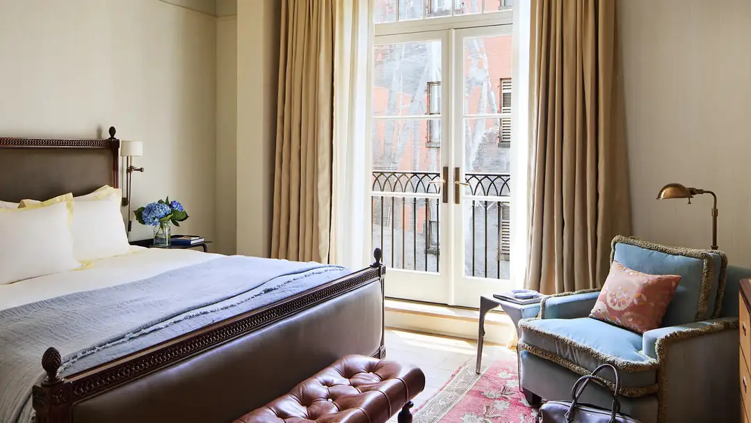 Courtyard King bedroom with a carved wood bed, a blue armchair and French doors to a small iron balcony